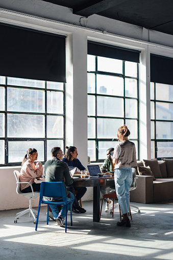 Group of young adults in casual attire collaboratively working and discussing projects in a bright co-working environment.