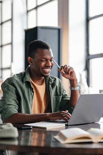 Smiling young man using a laptop in a bright co-working space, exuding focus and productivity.