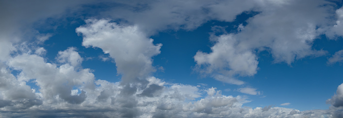 Panoramic view of a bright blue sky filled with fluffy white clouds. The clouds vary in size and are spread across the sky, suggesting a vast open atmosphere. The blue of the sky is a clear, vibrant hue that suggests a sunny day. There is a serene and tranquil quality to the scene, which may evoke feelings of calmness and openness.