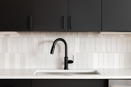 A kitchen faucet detail with black cabinets, a vertical subway tile backsplash, and a black faucet on a white marble countertop.