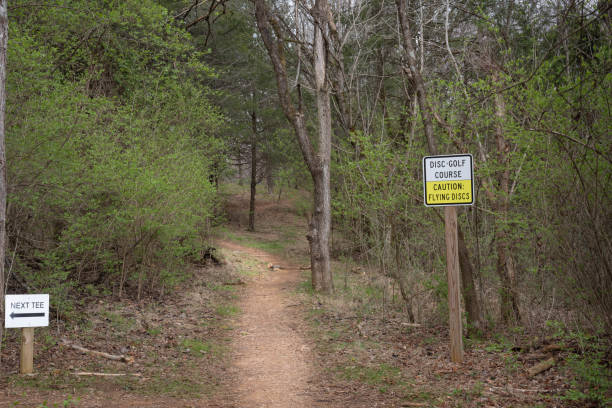 istock Disc-golf course.  Caution:  Flying discs and next tee signs near a trail in a park. 2094410512