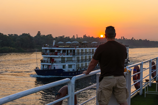 Man on his back leaning over the white railing of cruise in the Nile river looking at sunset