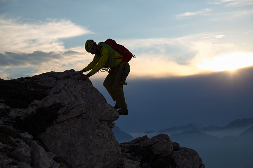 Mountain climber with climbing equipment (rope, backpack, helmet, hood,...) against the sunset. Climbing up the mountain.