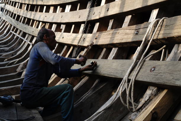 Volunteer craftspeople working on a reconstruction of a wooden Anglo-Saxon longship at The Longshed on the quay in Woodbridge, Suffolk, Eastern England. Woodbridge is close to Sutton Hoo, where, in 1939, the remains of an Anglo-Saxon royal ship burial were unearthed along with extraordinary treasures.