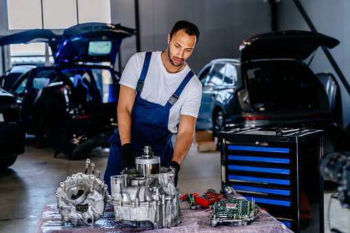 Electric car engine removed from car for repair. Arabian man use voltmeter working Internal Permanent Magnet Synchronous Reluctance Motor. Service maintenance of industrial to engine repair.