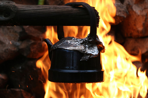 A grey kettle cooking on a campfire with flames surrounding it.