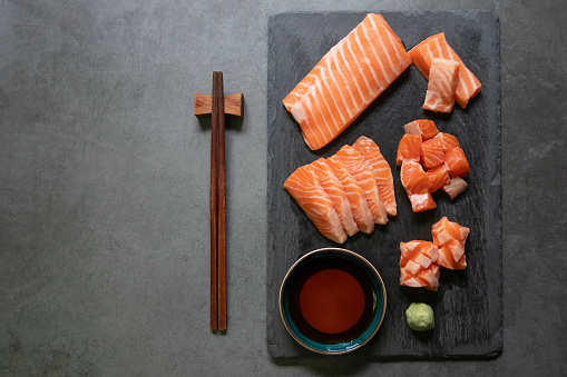 Salmon sashimi slices on black plate with chopsticks and shoyu, top view and copy space.