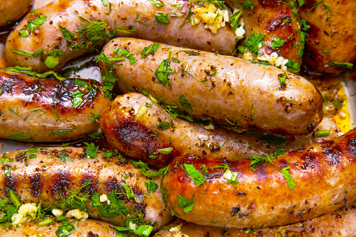 Grilled sausages with onions and garlic, sprinkled with parsley and dill closeup.