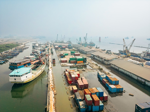 Aerial photo of wooden boats moored beside the pier at Sunda Kelapa, the historic port of Jakarta, Indonesia showing waterways and containers.
