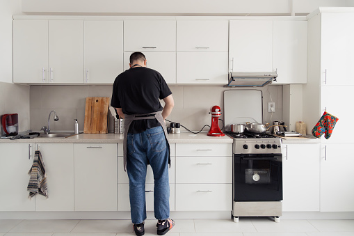 Back view of a man busy cooking in a well-equipped, bright kitchen.