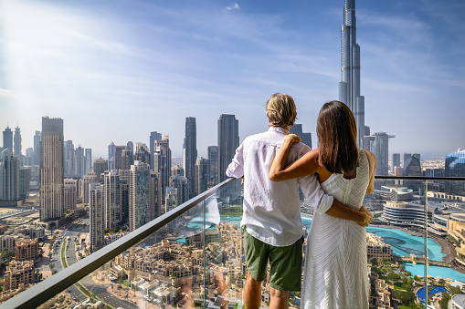 A hugging tourist couple on a balcony enjoys the elevated view of the skyline of Downtown Dubai, UAE