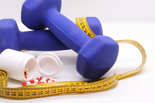 Close-up of dumbbells for sports and capsules with synthetic food supplements and measuring tape