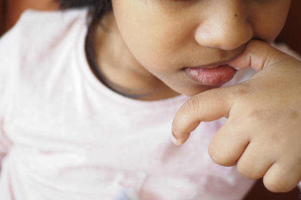 Cute 3 year old girl looking over the edge of a large mixing bowl as she learns how to prepare chocolate chip cookie dough at a kitchen table.