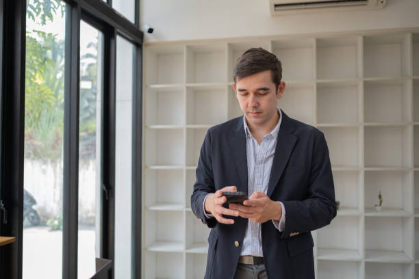 istock Happy business man talking on mobile cell phone device looking away standing at work, handsome businessman talking on his phone in office 2094576244
