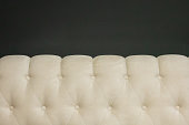 Close-up of a bed headboard with light-colored upholstery against a dark wall. Form. Background. Texture.