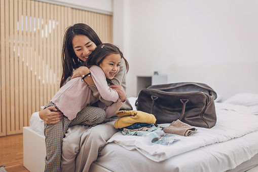 Two people, Japanese woman with her little daughter hugging in hotel room.