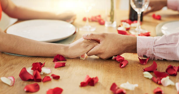 istock Couple, roses and holding hands on dinner date, anniversary or valentines day dining by table at home. Closeup of man and woman in celebration or care for romantic honeymoon, embrace or love at house 2094660070