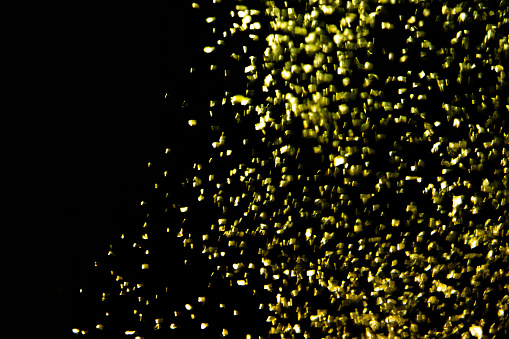 Gold confetti glittering wave. Golden sparkling on black background. Shiny wavy crumbs, golden texture.