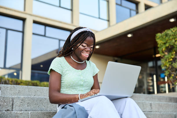 istock Happy young black female student with vitiligo on her skin using laptop computer sitting on the stairs of the university. Concept of youth culture and technology 2094667259