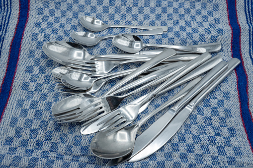 Cutlery on a dishcloth. Knives, forks, small and large spoons lie in a disarray on a tea towel