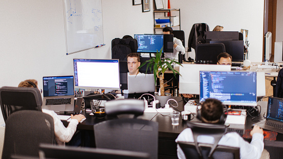 Group of male and female Caucasian computer programmers working together on a computer at the open space office