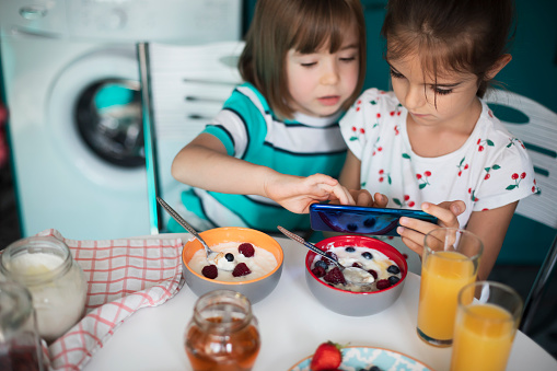 Little cute children using smartphone while having breakfast. Healthy breakfast.
