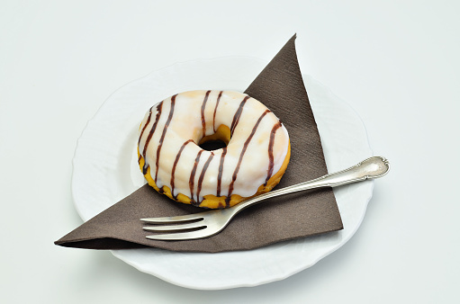 striped donut on white plate with fork and brown napkin,  close up, isolated on white background