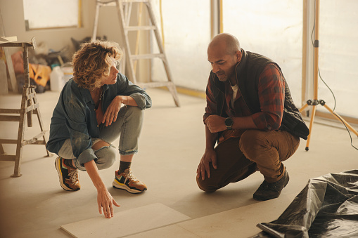 Man and woman working together on renovating their home, discussing upgrades for their kitchen flooring. They use their DIY skills redesign and improve the space, focusing on tile selection.