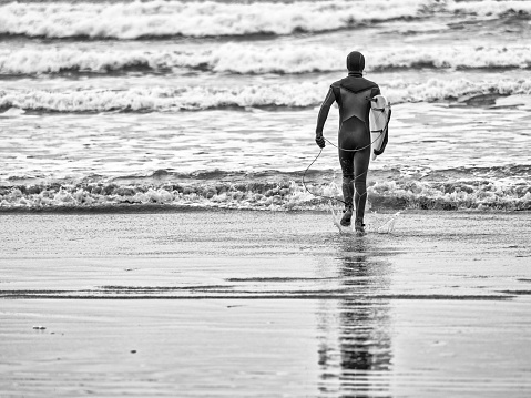 Young unrecognizable male entering the water for a surfing session at Pacific Rim National Park on Vancouver Island at sunset, British Columbia