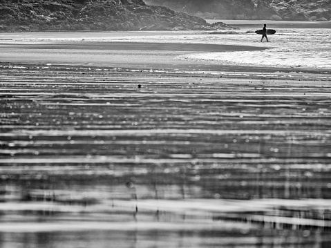 Young unrecognizable male entering the water for a surfing session at Pacific Rim National Park on Vancouver Island at sunset, British Columbia