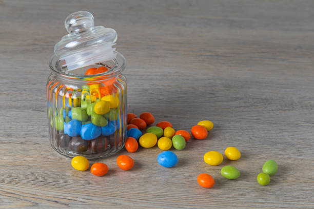 Peanuts in multi-colored icing in a glass jar on a wooden table