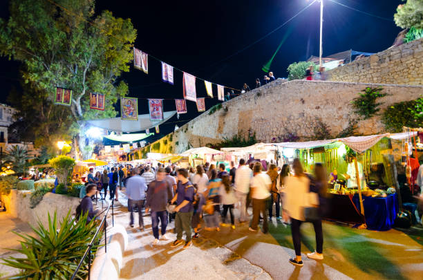 5th August, 2014 - Ibiza Town, Spain: The streets of Ibiza's Old Town, Dalt Vila, come alive during the Medieval Festival, transforming the historic area into a vibrant tableau of the past. Tourists, shoppers, and stall merchants mingle among the colorful stalls, showcasing everything from traditional crafts to local delicacies, against the backdrop of the ancient city's charming architecture. This annual event not only celebrates the rich history of Ibiza but also brings together people from all walks of life to partake in the festivities.