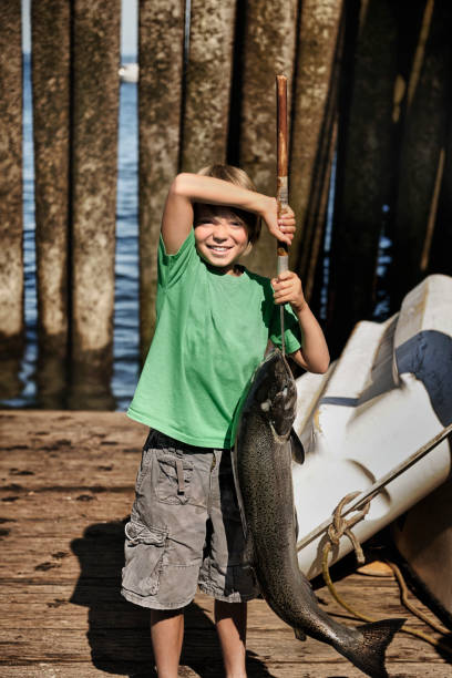 A vertical shot of a child proudly displaying a big fish on a dock