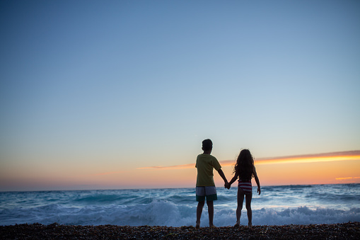 Woman with her little son on the beach by the sea in sunset, they are on vacation.