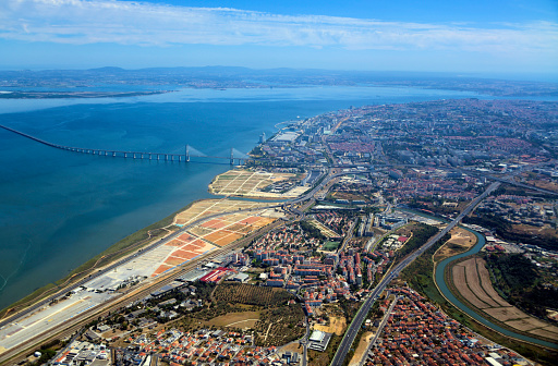 Lisbon, Portugal: aerial view of the 'Mar da Palha' (Sea of Straw) inland sea in the Tagus River estuary, the eastern area of Lisbon and the Montijo / Alcochete on the southern bank, connected by the Vasco da Gama bridge. At the bottom the River Trancão can be seen, meandering towards its mouth, separating Bobadela from Sacavém. Above the bridge lie the Expo, Moscavide and Olivais areas. On the horizon is the south bank, with the Arrabida mountains and the Montijo Air Force base (BA6) on the top left