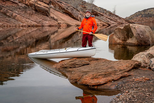 senior male paddler with a decked expedition canoe with a wooden paddle on a rocky shore of Horsetooth Reservoir near Fort Collins, Colorado, low water level fall or winter scenery - self portrait