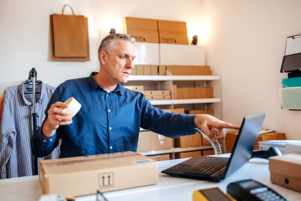 istock Man packing goods and preparing it for delivery service using laptop for checking orders 2094909408