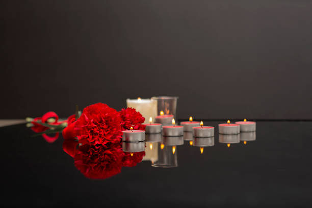 istock Red flowers carnation and many burning candles on a black surface, selective focus on the one candle. 2094932288