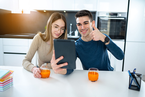 Young couple talking with family on video call and showing thumbs up