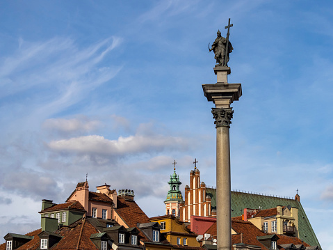 Sigismund III Vasa Column with few buildings of the Old Town on the background. Blue sky, slightly covered with clouds. Vibrant colors of old European architecture.