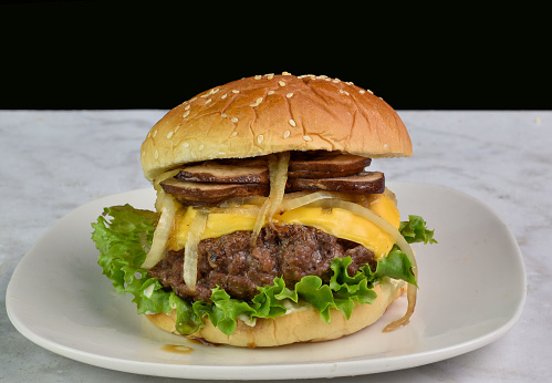 cheese burger top with onions and mushrooms  on a sesame bun