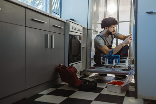 Photo of young handyman fixes dishwasher. Handyman service
