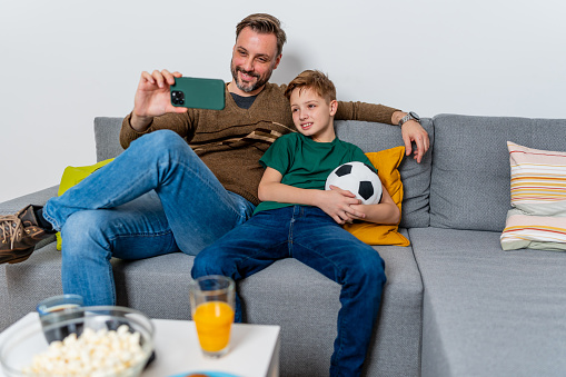 A father and son crowd around a smartphone, their passion for the soccer game unfazed by the screen's size, as they share a moment of bonding