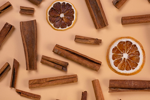 background with cinnamon sticks and dried lemon or orange slices on a beige background, cozy food, spicy trendy background.