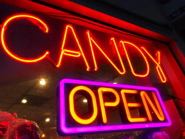 A neon sign at a candy store, along with an "open" sign in the window