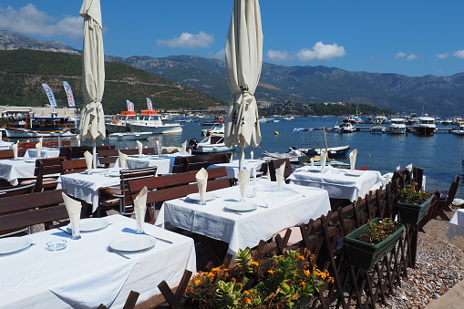 Budva, Montenegro 8.15.22 Adriatic sea Mediterranean riviera. Tourism business. Yachts, boats and pleasure craft. Restaurant by the sea, first line. Tables, chairs, sun umbrellas and white tablecloths