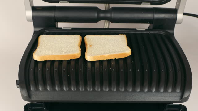 Toasting bread in the electric grill. Women's hands place bread on the grill. The concept of toasting bread.