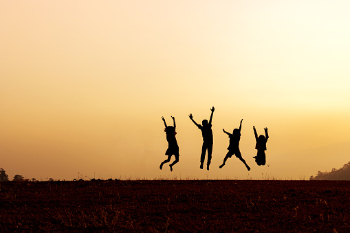 Silhouette group of happy children jumping playing on mountain at sunset, summer time