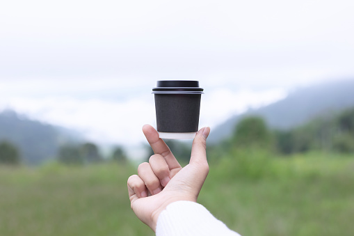 Female hand holding coffee cup on misty mountains landscape.