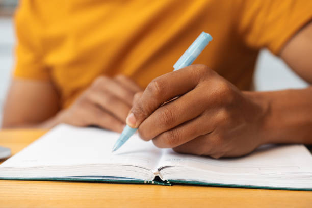 istock African American man is holding pen, taking notes while sitting at table, selective focus on hands 2095247762